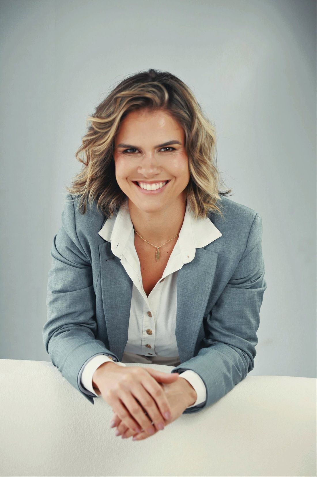 Dra. Merabe Muniz sorrindo, de blazer, com os braços apoiados